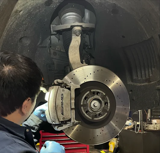 Professional brake service showing AMG performance brake system with drilled rotors and calipers